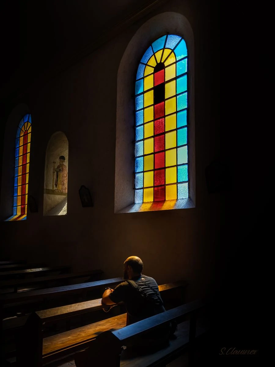 Personne assise sous la lumière colorée des vitraux